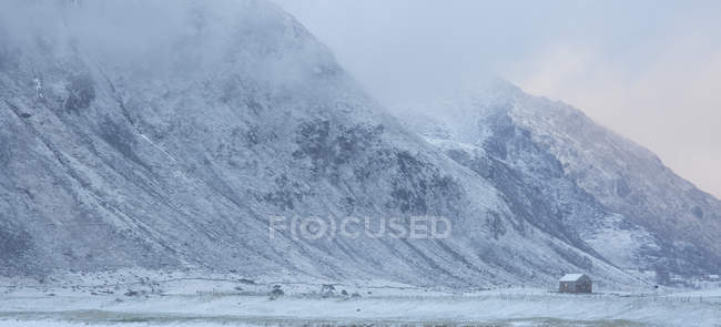 Montaña cubierta de nieve y cabaña remota Flakstad Lofoten Noruega - foto de stock