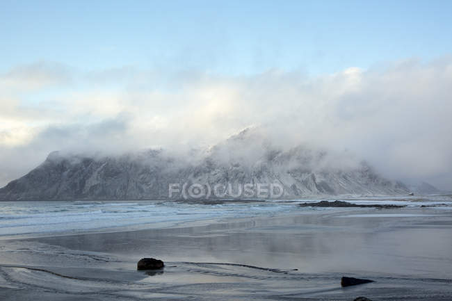 Nubes sobre nieve cubierta montaña océano Skagsanden Lofoten Noruega - foto de stock