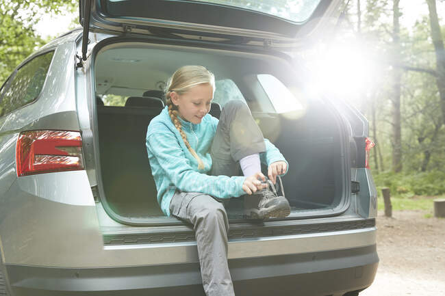 Girl preparing for hike at back of car tying shoes — Stock Photo