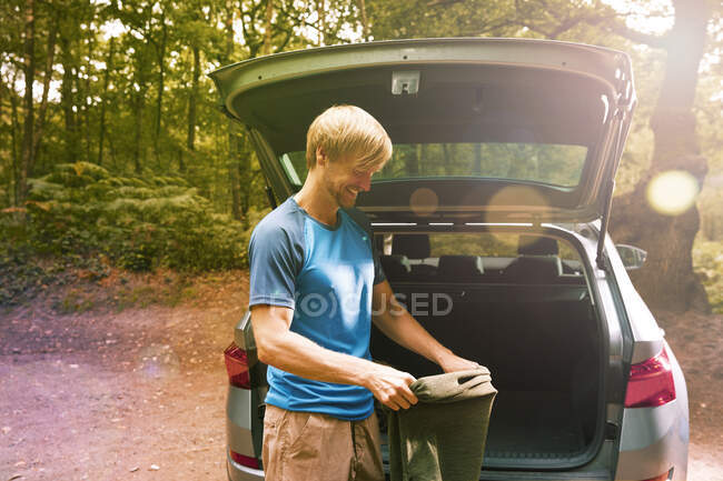 Smiling man preparing for hike at back of sunny car — Stock Photo