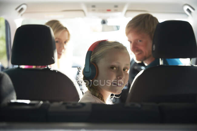 Retrato chica sonriente con auriculares cabalgando en el asiento trasero del coche - foto de stock