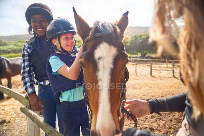 Meninas felizes aprendendo cavalgadas no ensolarado paddock — Fotografia de Stock
