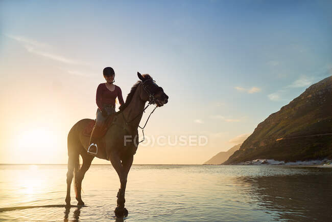 Portrait jeune femme équitation sur tranquille coucher de soleil océan plage — Photo de stock