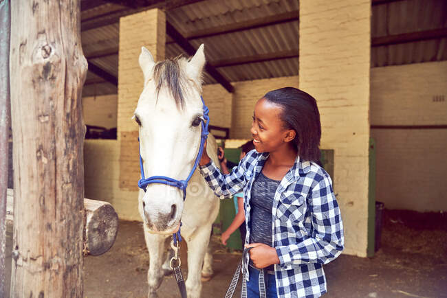 Happy girl petting horse outside stables — Stock Photo