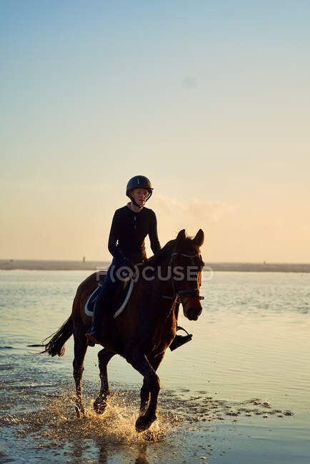 Young woman horseback riding in ocean surf — Stock Photo