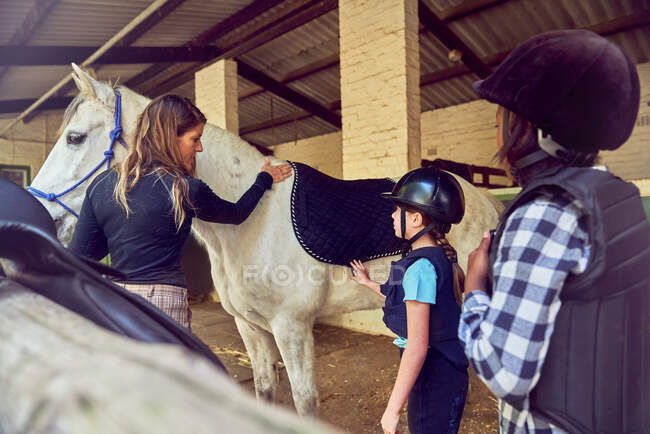 Female instructor helping girls prepare for horseback riding — Stock Photo