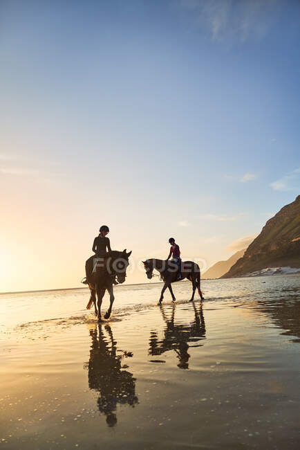 Young women horseback riding on tranquil sunset beach — Stock Photo