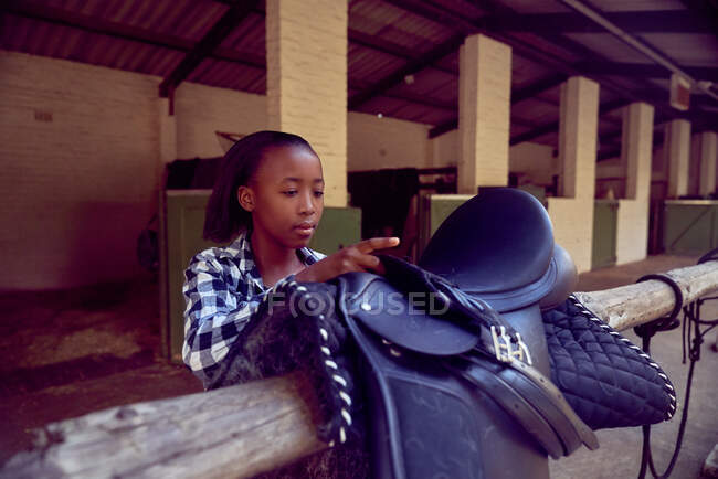 Chica preparando silla de montar a caballo fuera de establos - foto de stock