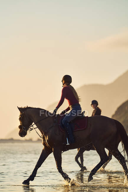 Jovem mulher cavalgando na praia do oceano ao pôr do sol — Fotografia de Stock