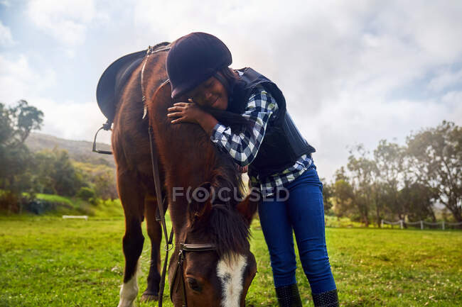 Happy girl hugging horse in rural grass paddock — Stock Photo