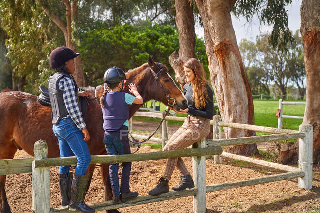 Instrutora e meninas acariciando cavalo na ensolarada doca rural — Fotografia de Stock