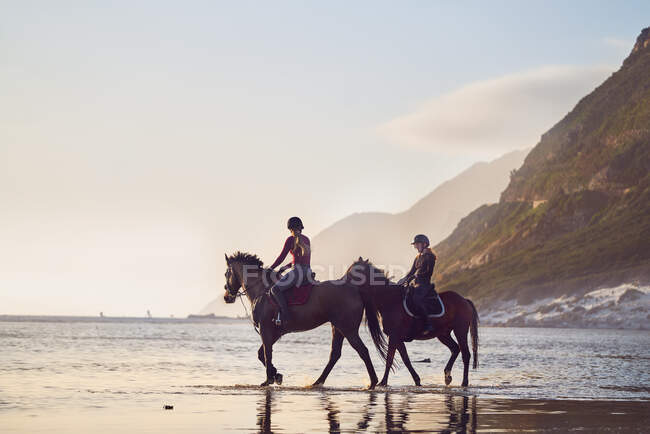 Jovens mulheres cavalgando na tranquila praia oceânica — Fotografia de Stock