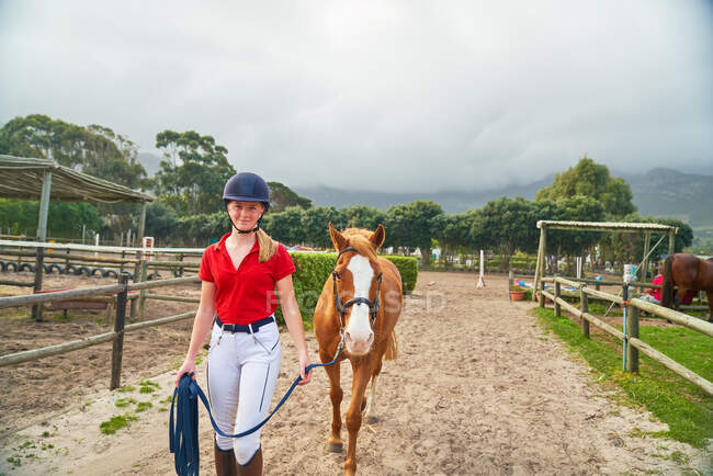 Retrato confiante adolescente levando cavalo ao longo de piquetes rurais — Fotografia de Stock