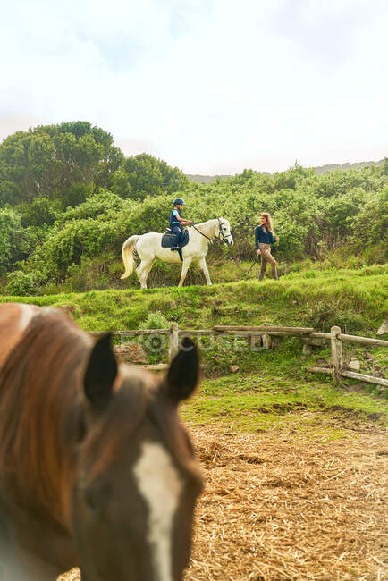 Frau führt Mädchen hoch zu Ross über Pferdekoppel — Stockfoto