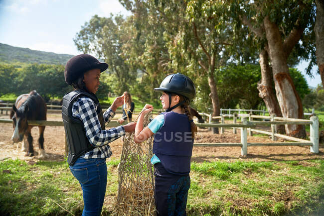 Happy girls carrying hay toward horses in paddock — Stock Photo