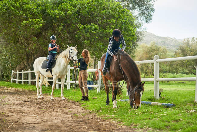 Chicas preparándose para la clase de equitación en el paddock rural - foto de stock