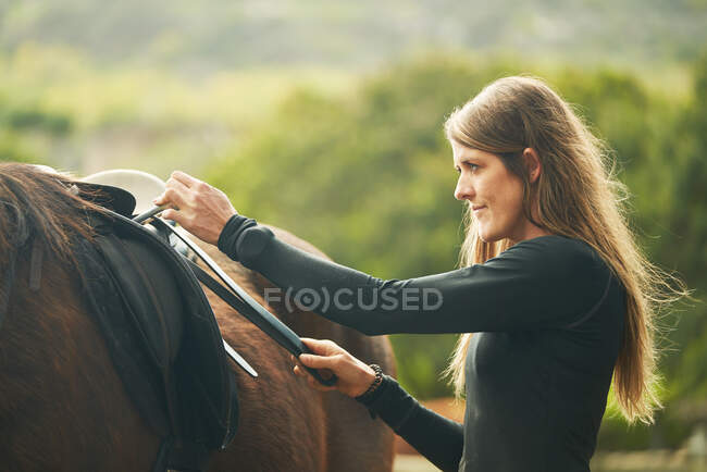 Woman preparing saddle for horseback riding — Stock Photo