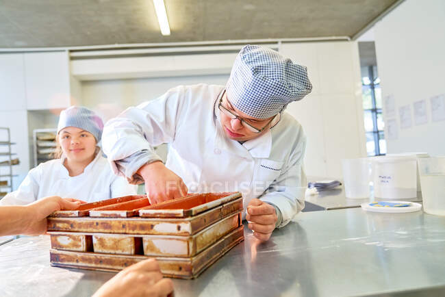 Joven estudiante masculino con síndrome de Down horneando pan en la cocina - foto de stock