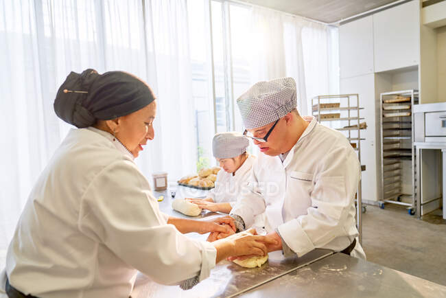 Chef ayudando a los estudiantes de Síndrome de Down rollo de masa en la cocina - foto de stock