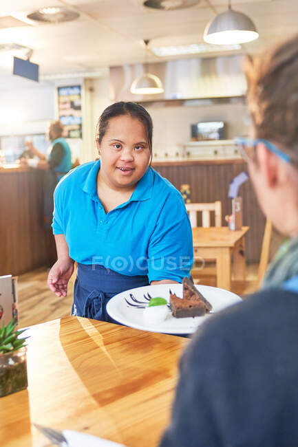 Молодая женщина с синдромом Дауна подает десерт в кафе — стоковое фото