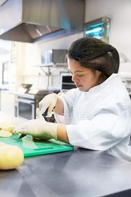 Focused young woman with Down Syndrome cooking in cafe kitchen — Stock Photo