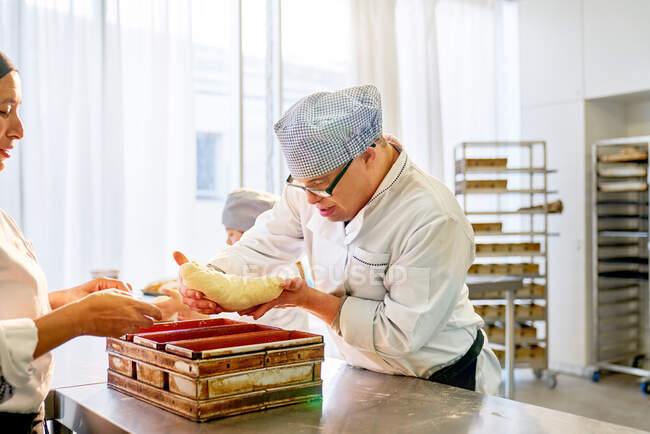 Сосредоточенный молодой студент с синдромом Дауна печет хлеб — стоковое фото