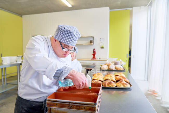 Сосредоточенный молодой человек с синдромом Дауна печет хлеб на кухне — стоковое фото