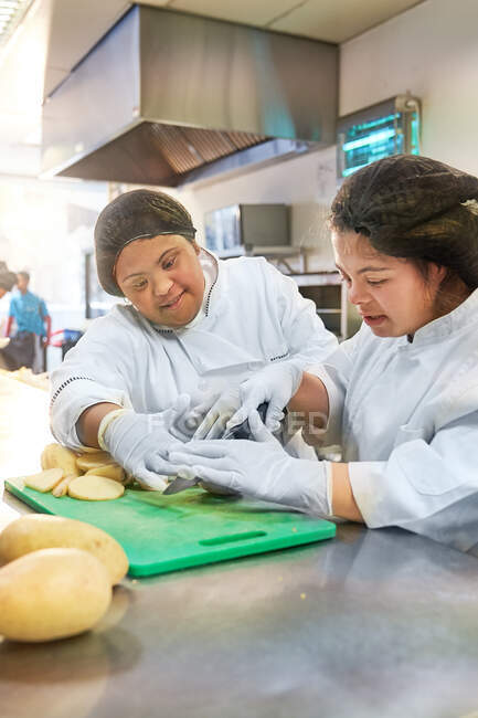 Jeunes femmes atteintes de trisomie 21 coupant des pommes de terre dans la cuisine du café — Photo de stock