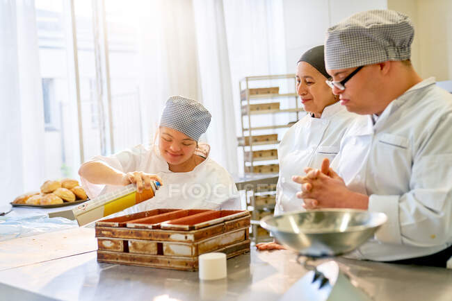 Chef y estudiantes con síndrome de Down horneando pan en la cocina - foto de stock