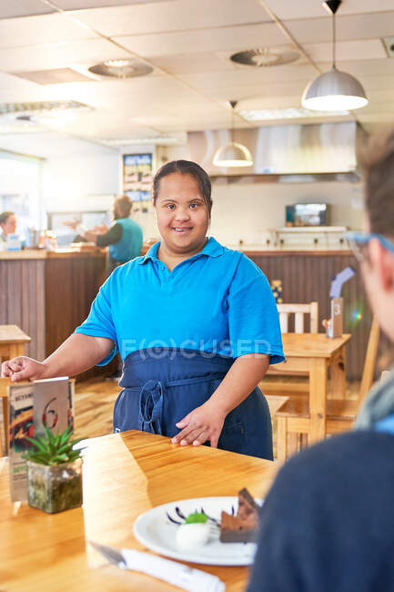 Portrait confiant jeune serveur féminin avec trisomie 21 dans un café — Photo de stock