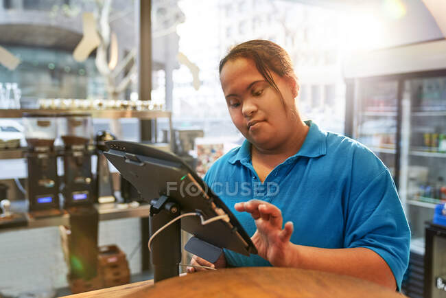 Junge Frau mit Down-Syndrom arbeitet an Kasse in Café — Stockfoto