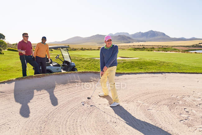 Старший мужчина стреляет из бункера на солнечном поле для гольфа — стоковое фото