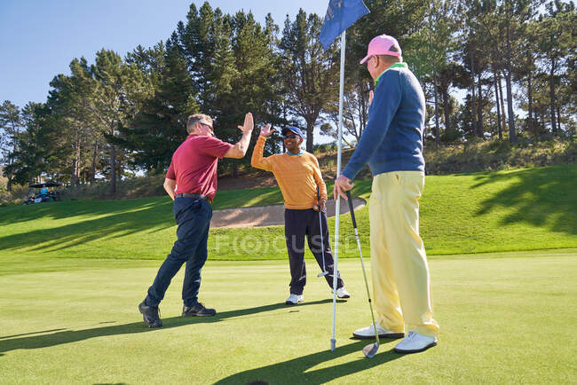 Amis masculins high fiving sur terrain de golf ensoleillé putting green — Photo de stock