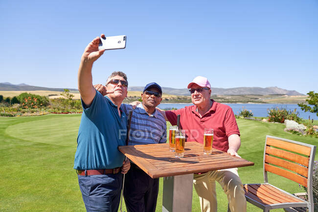 Amigos varones bebiendo cerveza y tomando selfie en el patio del campo de golf - foto de stock
