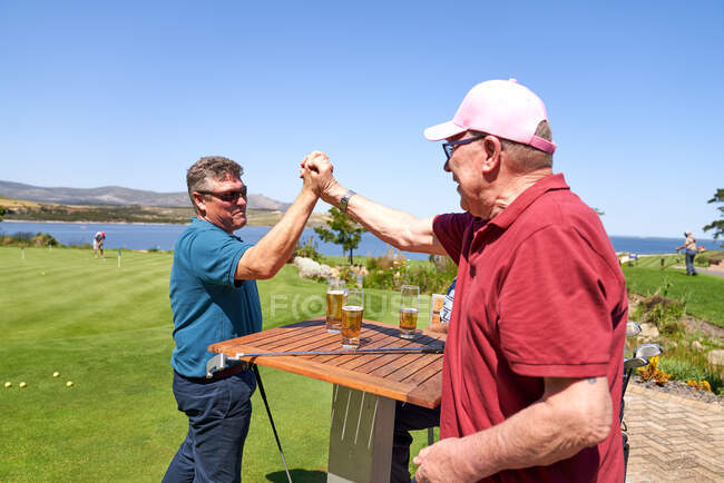 Счастливые друзья-гольфисты дают пять и пьют пиво. — стоковое фото