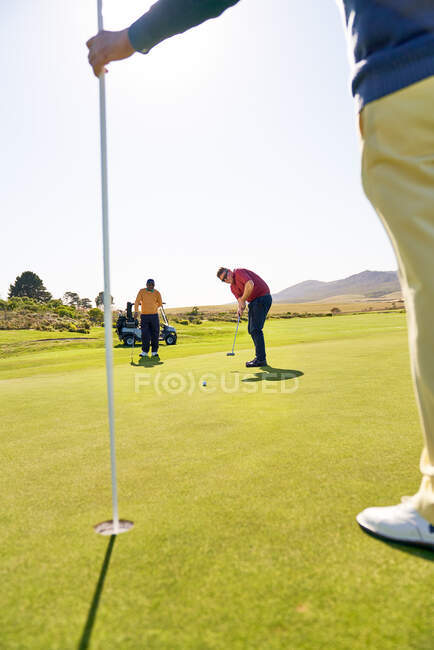 Чоловічий гольф прикладає до шпильки і лунки на сонячному полі для гольфу — стокове фото