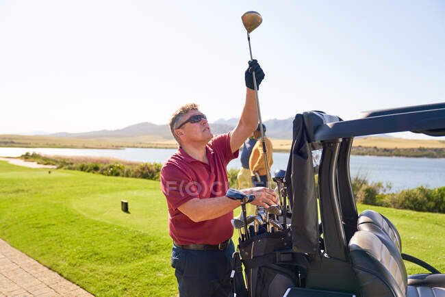 Чоловік-гольф вибирає гольф-клуб у коробці трійника на сонячному полі для гольфу — стокове фото