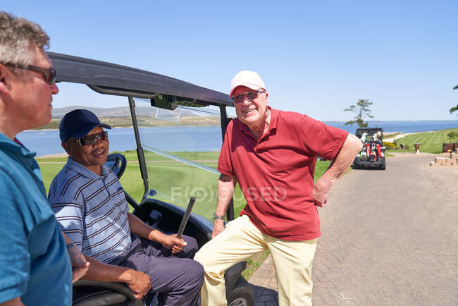 Felices amigos golfistas masculinos hablando en el carrito de golf en el campo soleado - foto de stock