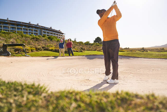 Golfista masculino tomando um tiro fora do bunker ensolarado — Fotografia de Stock