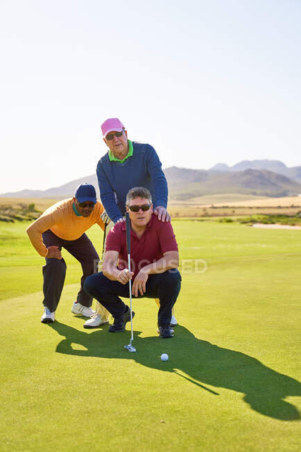 Male golfers planning putt shot on sunny golf course putting green — Stock Photo