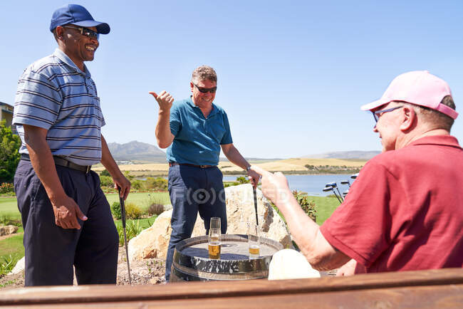 Happy male golfers talking and drinking beer at clubhouse patio — Stock Photo