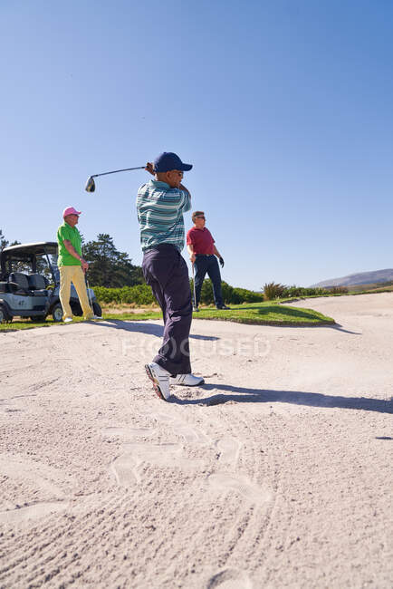 Male golfer taking a shot out of sunny golf bunker — Stock Photo