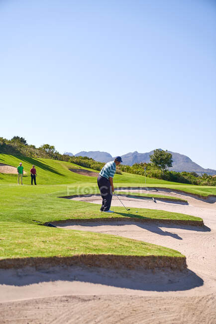 Homme golfeur se préparant à prendre un coup au-dessus du bunker de terrain de golf ensoleillé — Photo de stock