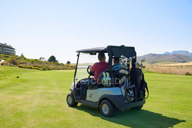 Male golfers driving golf cart on sunny golf course greens — Stock Photo
