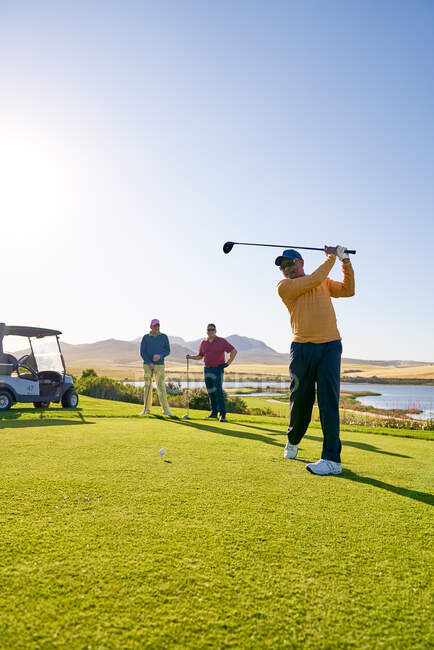 Male golfer teeing off at sunny golf course tee box — Stock Photo
