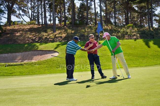 Golfistas masculinos apertando as mãos no campo de golfe ensolarado colocando verde — Fotografia de Stock