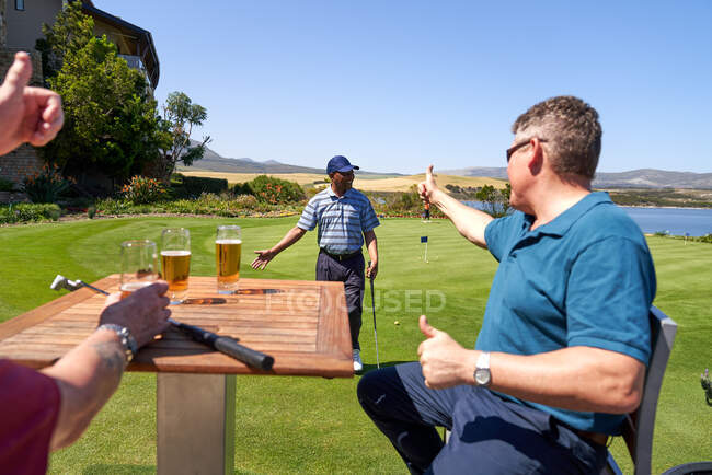 Male golfers drinking beer cheering friend on practice putting green — Stock Photo