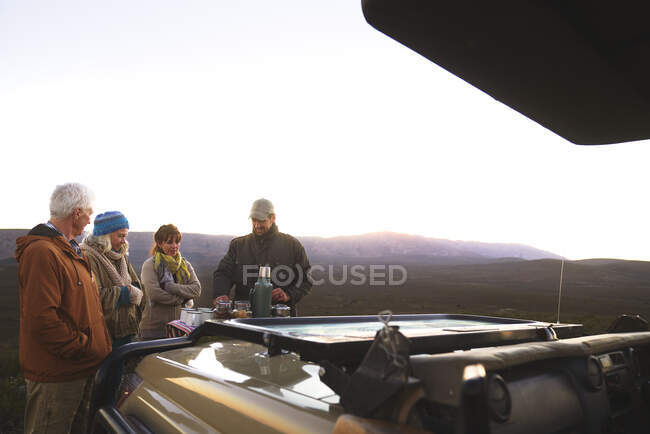 Safari tour guide and group enjoying coffee outside off-road vehicle — Stock Photo