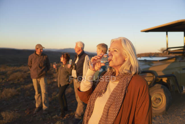 Mulher sênior em safari bebendo champanhe ao pôr do sol — Fotografia de Stock