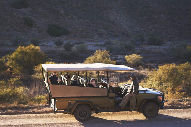 Safari guía turístico y grupo en vehículo todoterreno en el camino de tierra soleado - foto de stock